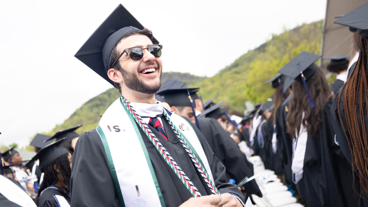 A graduate wearing sunglasses smiles broadly