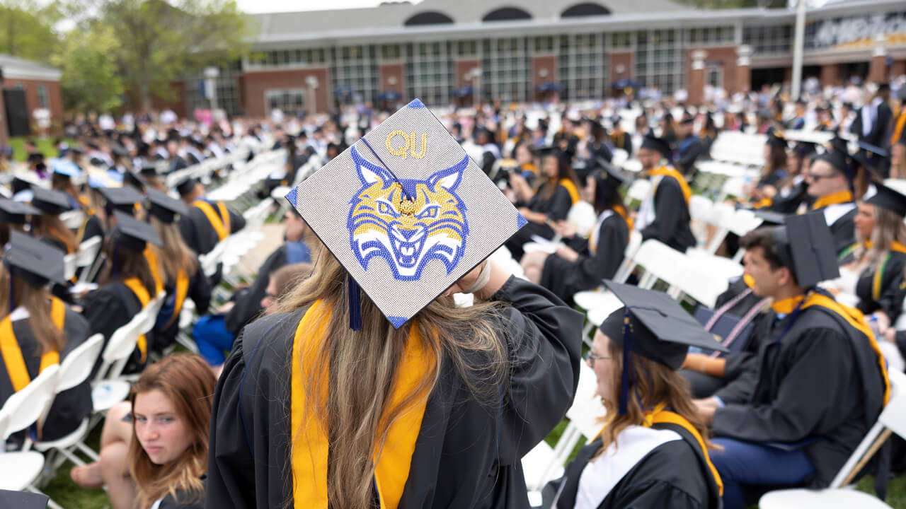 A graduate wears a cap decorated with the Quinnipiac bobcat logo