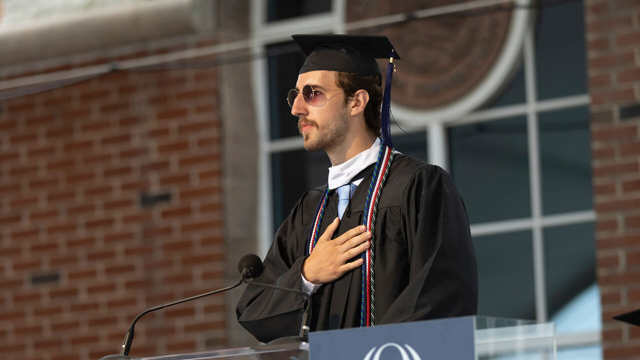 Lachlan Harvey stands and speaks at a podium on the Commencement stage