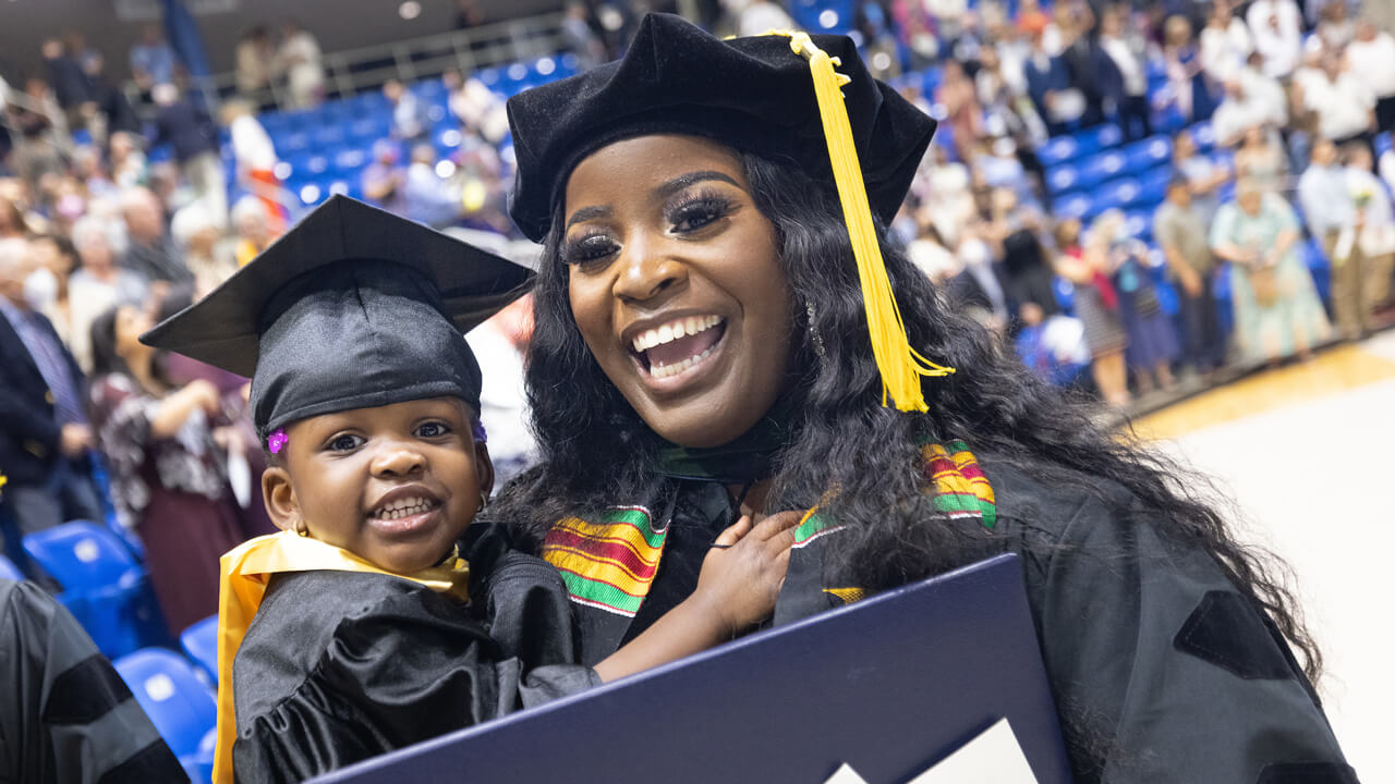 A medical graduate holds up her baby girl and her diploma in celebration