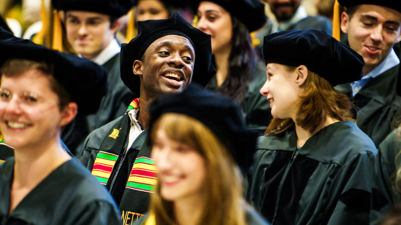Two graduate students speak to each other in audience during commencement