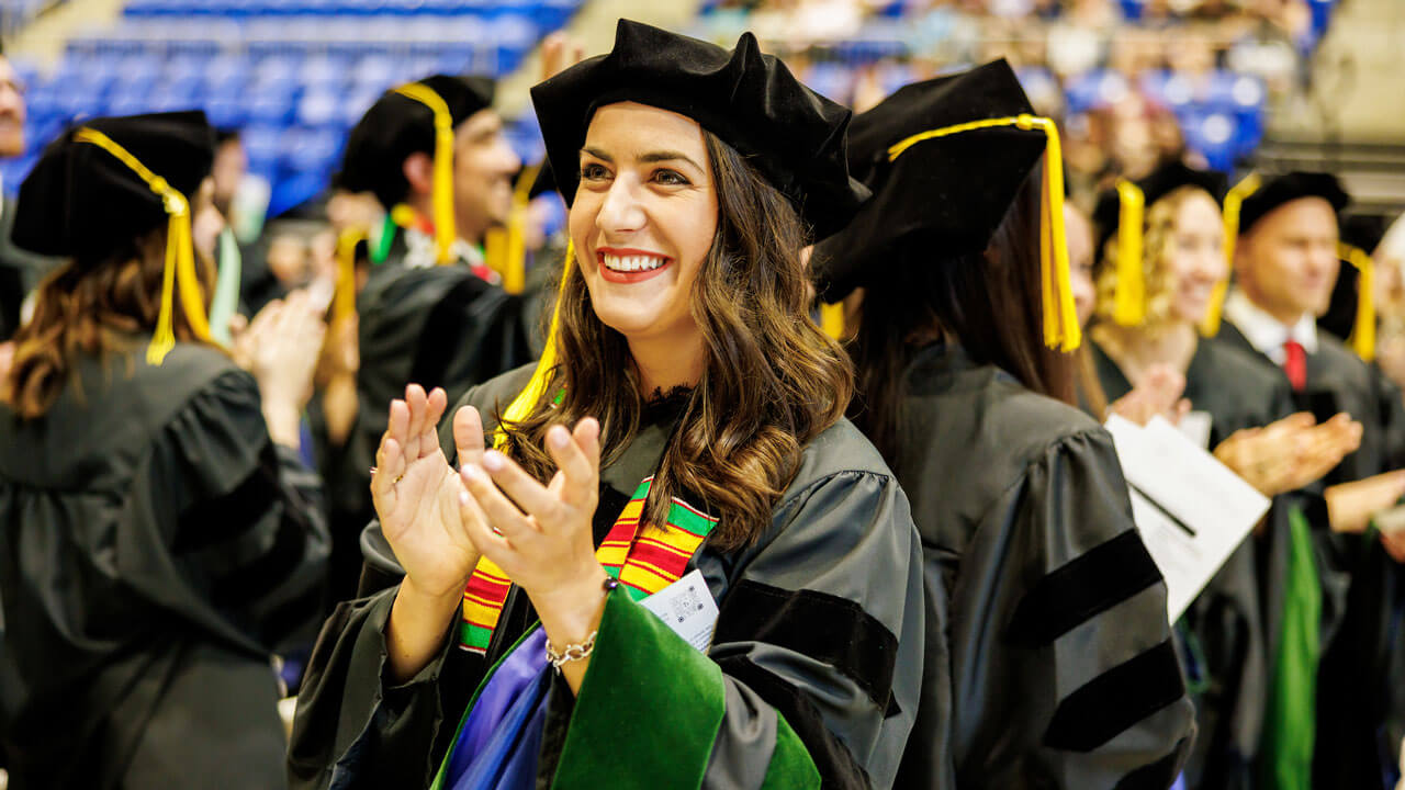 A group of graduate medical student applauds during commencement
