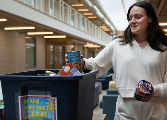 Marissa Roberge puts food in a "Be Kind LEave Your Food Behind" bin
