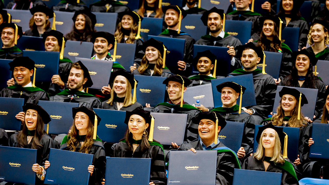 A sea of graduates hold up their diplomas