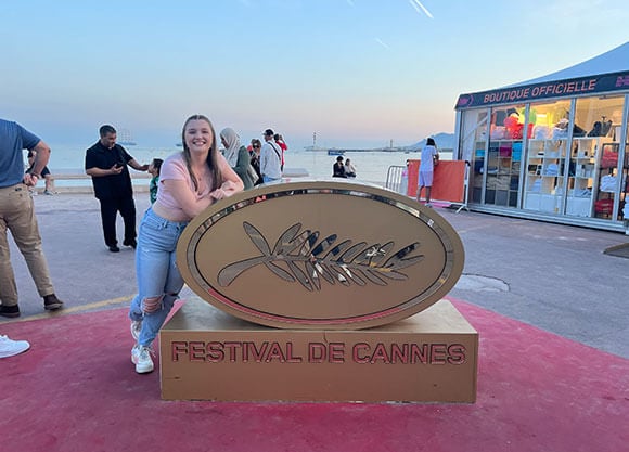 Girl leaning on Cannes Festival sign next to the ocean