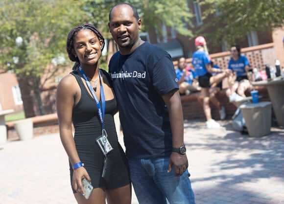 A student and their dad wearing a Quinnipiac Dad shirt smile for a photo during move in