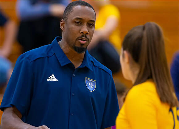 Coach Kyle Robinson talks with a volleyball player on the court