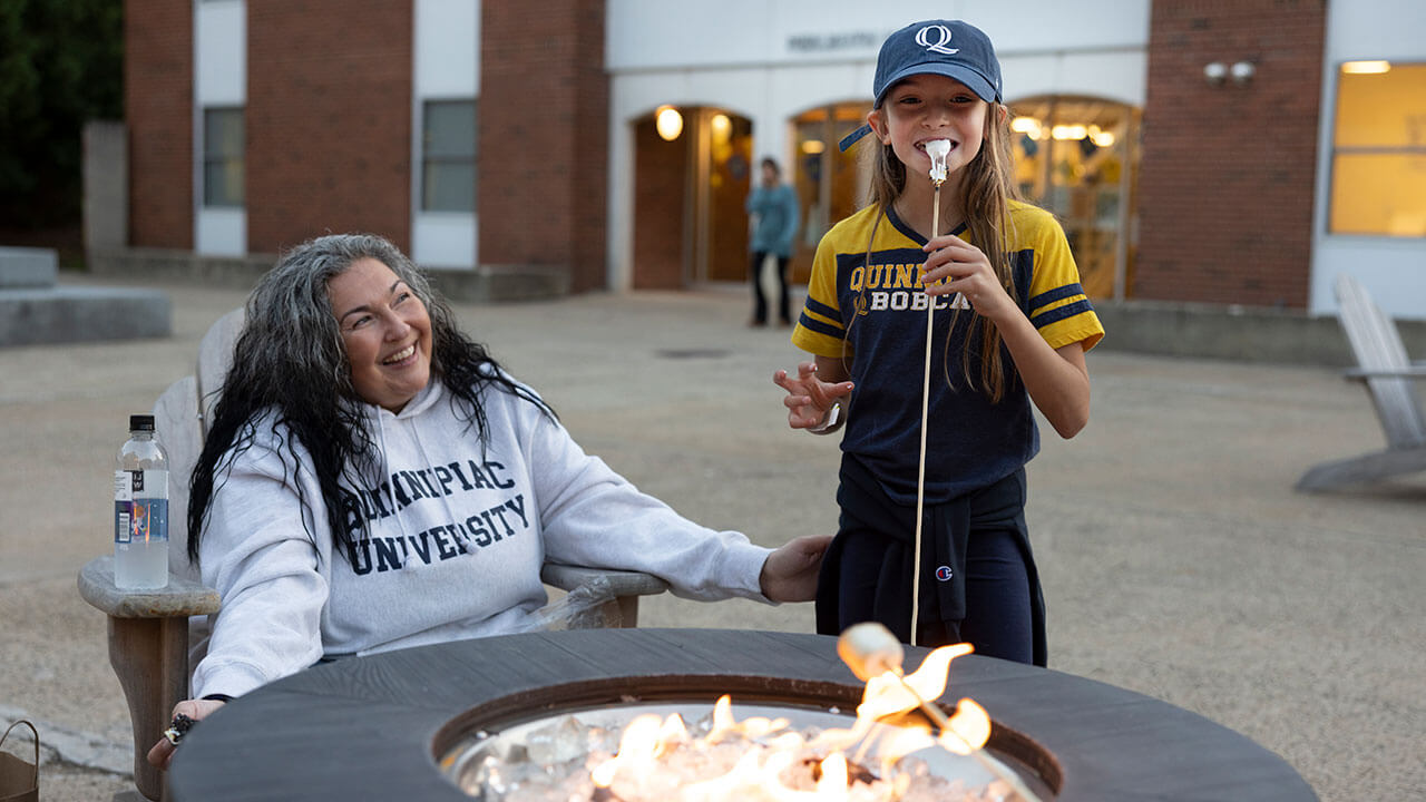 A mother and child toast marshmallows in front of an outdoor fire pit