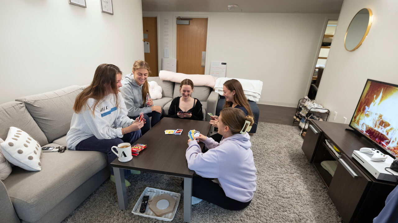 Friends play cards at a couch and coffee table in their common room