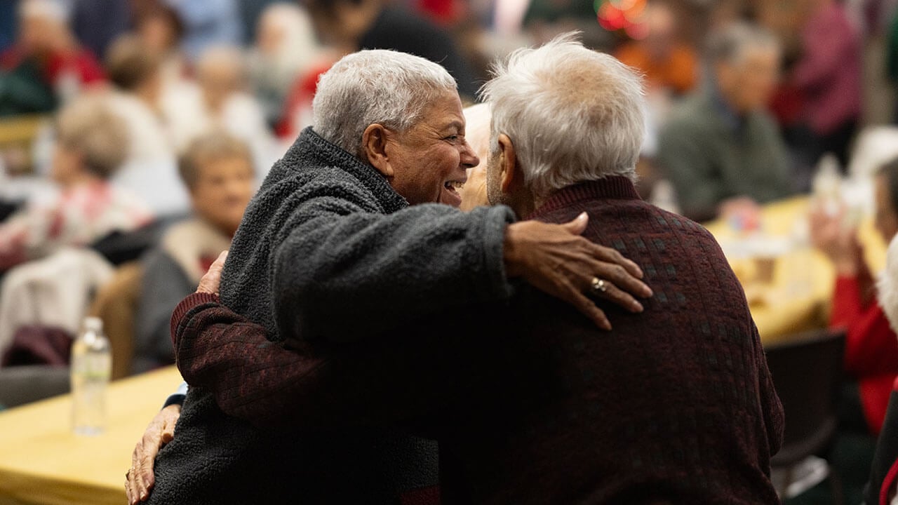 Two senior citizens embrace in a hug.