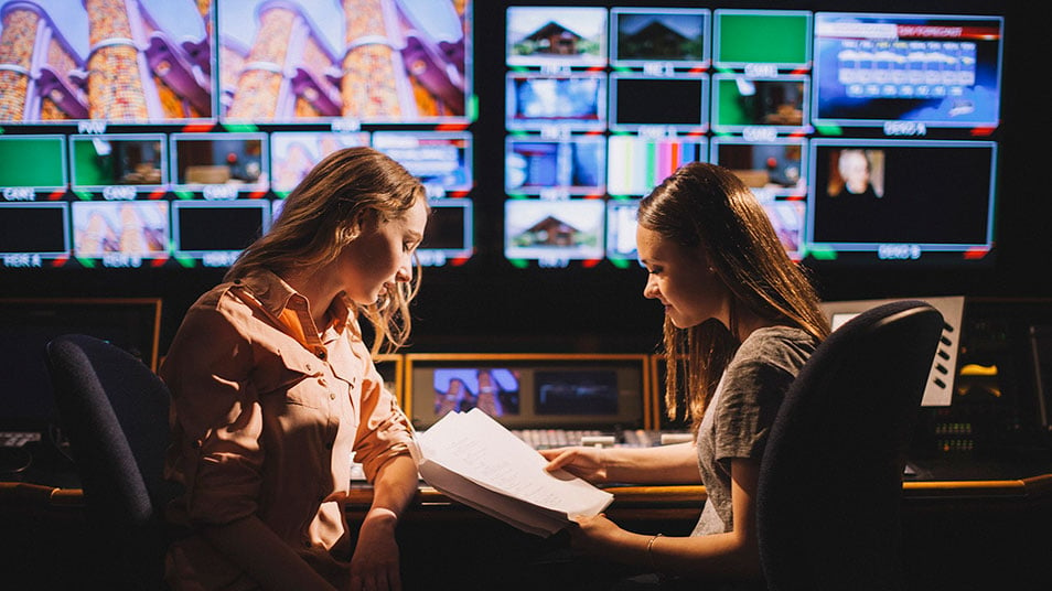 Two students go over notes together as they sit in the control room of QU's television studio