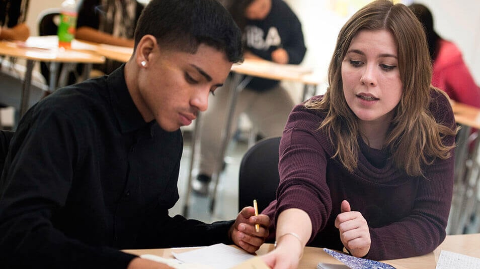 A School of Education student points at a high school student's spiral bound notebook