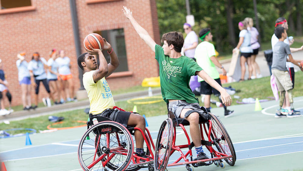 Two teenagers with limb loss play basketball using wheelchairs
