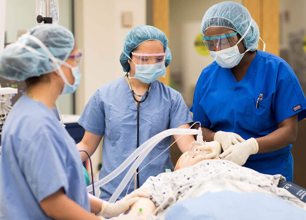 Nursing students in scrubs practice treatment on a medical mannequin in an operating room