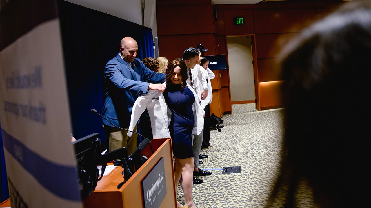 Students on stage getting their white coats put on them.