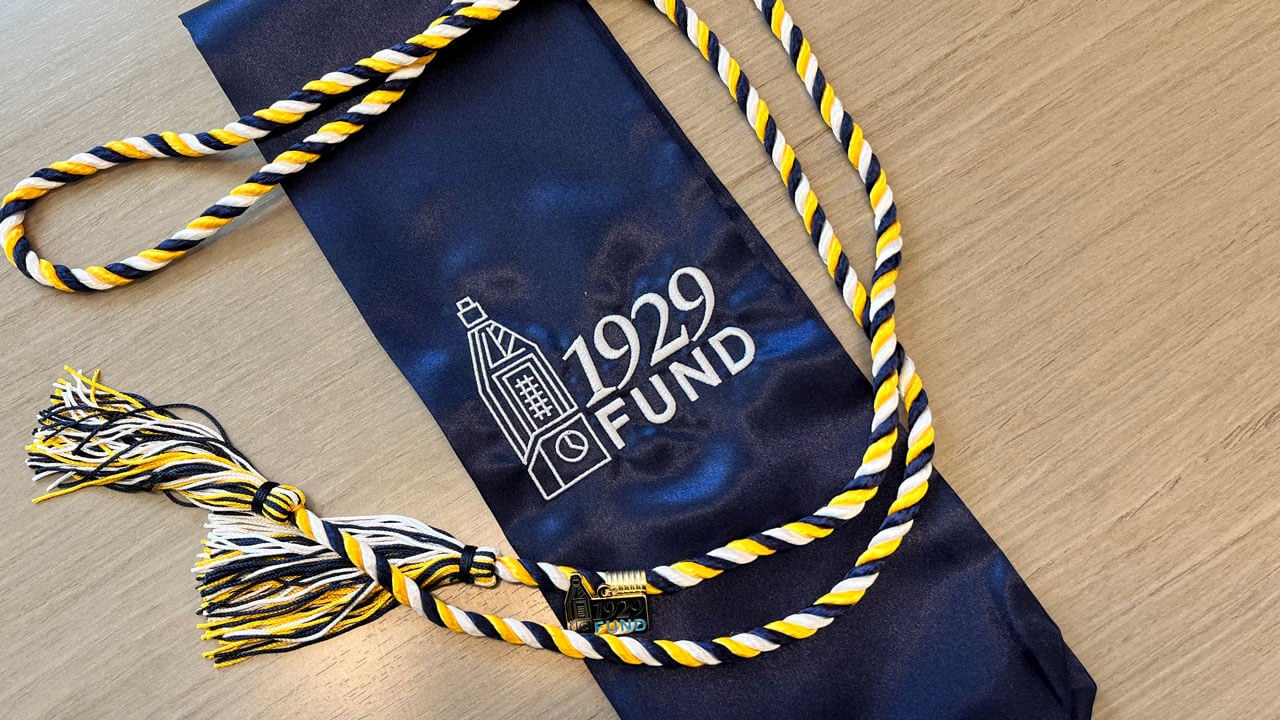 Photo of a navy stole with white lettering that reads 1929 Fund with yellow and blue graduation chords