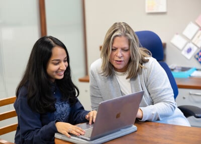 A student and professor talk together with a laptop