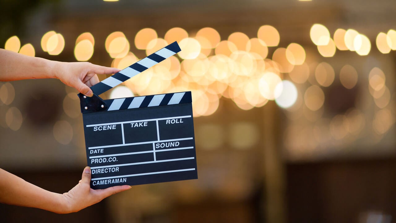 Hands holding a film slate with gold lights in the background.