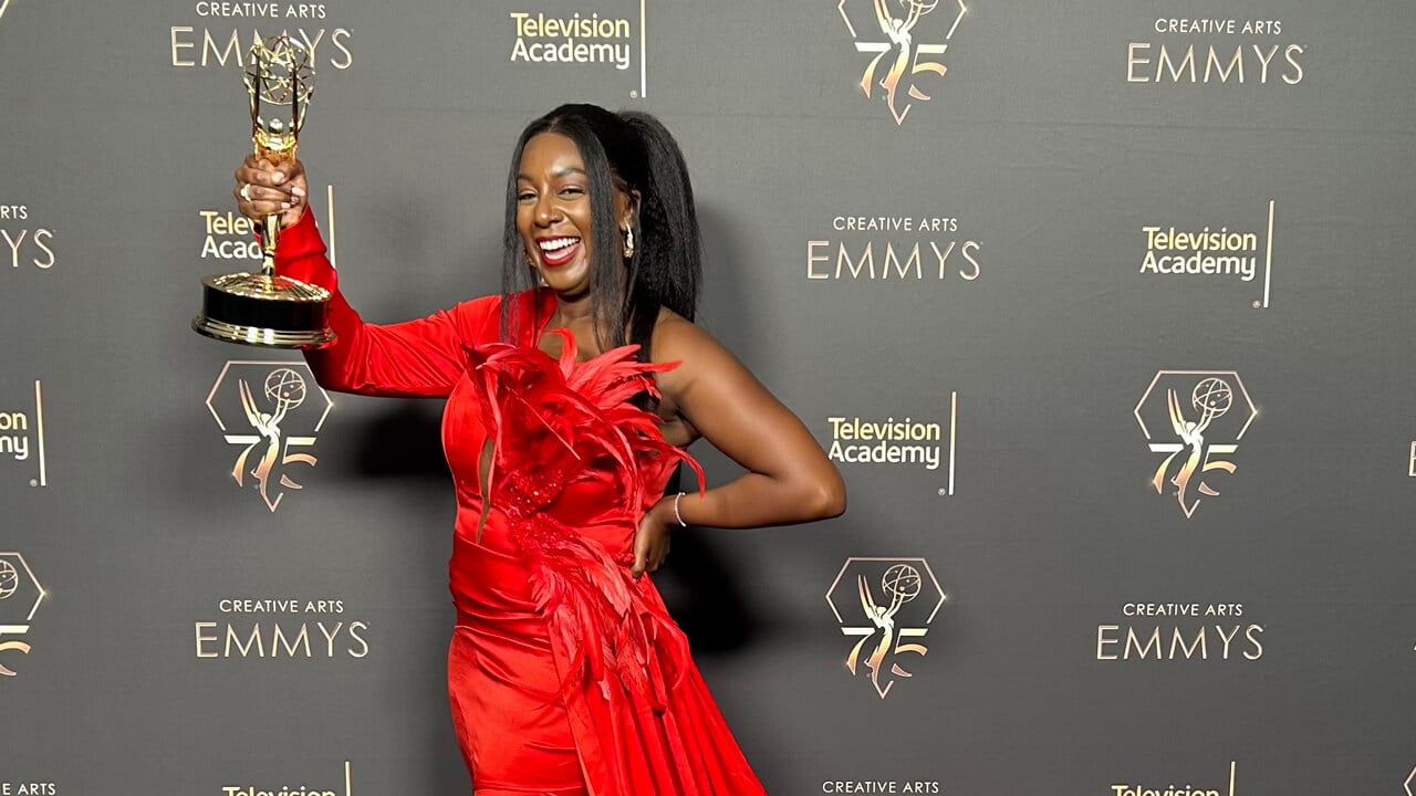 Jazzy Collins poses in a red dress with her EMMY trophy in front of the EMMYS step and repeat