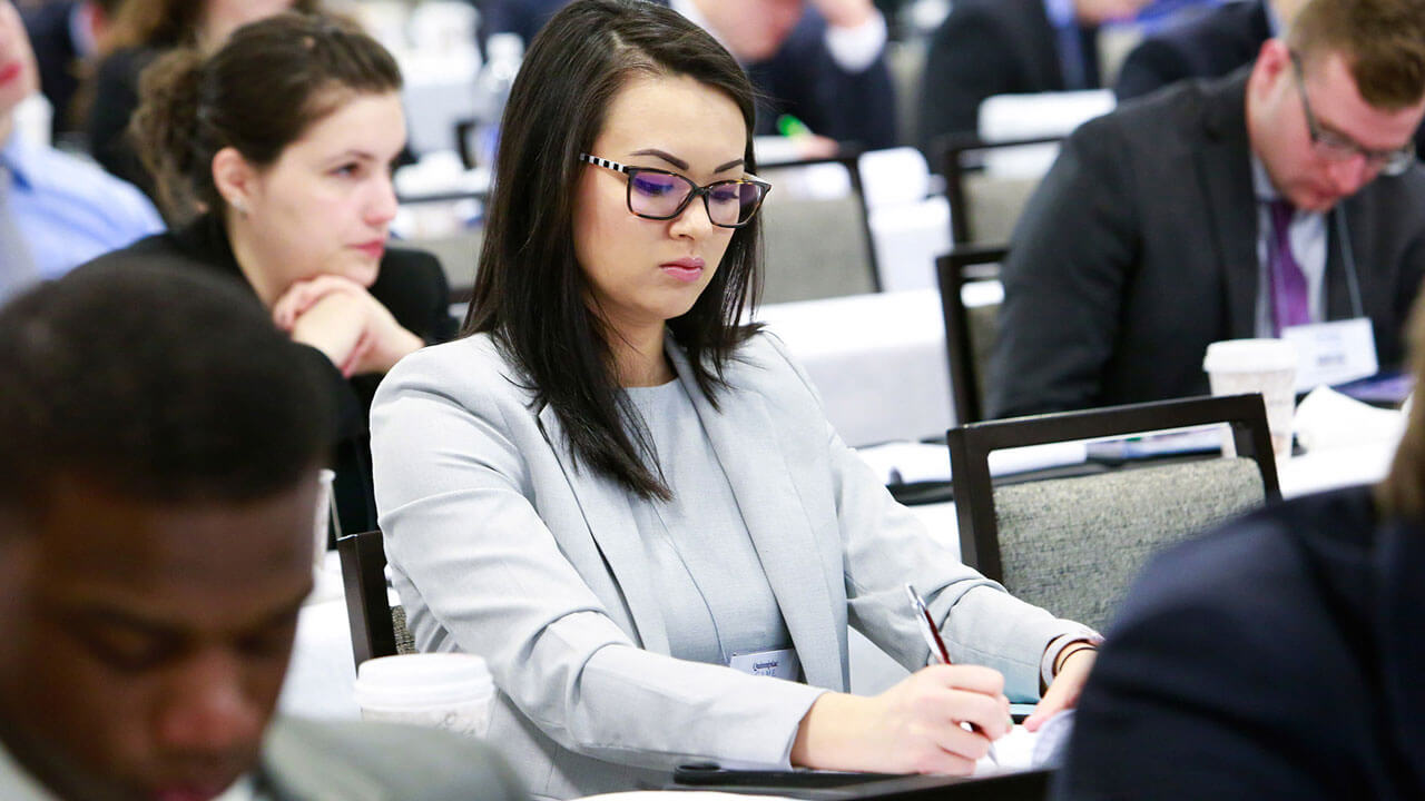 A student sits at a participant table taking notes during GAME Forum