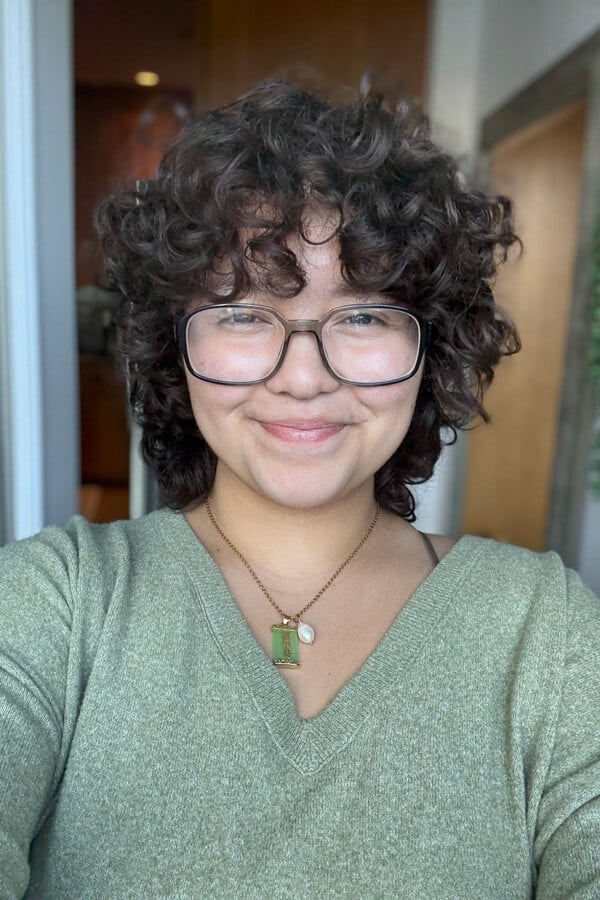 A vertical headshot of Aslin Argueta wearing a green sweater and glasses.