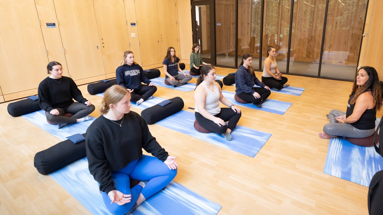 Students sit cross legged on yoga mats as they are led through a meditation exercise