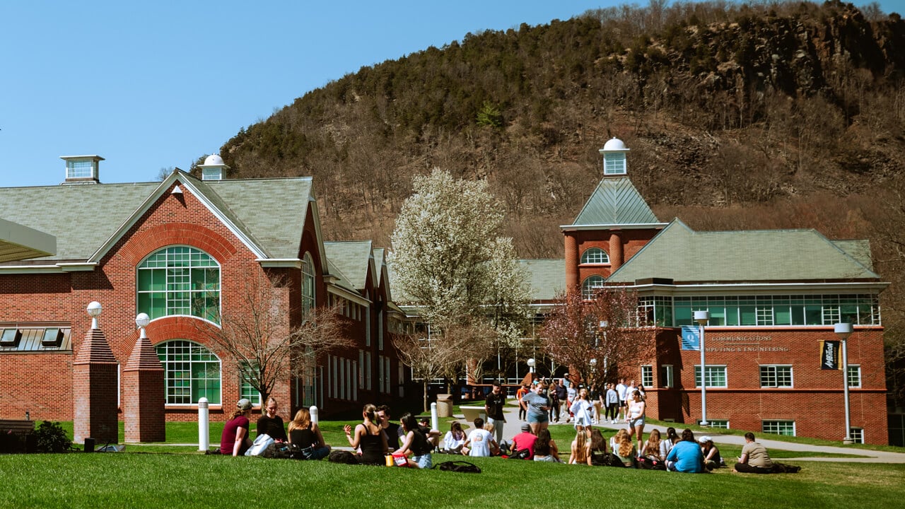 A class sits on the grass outside the Communications, Computing and Engineering building on a sunny day