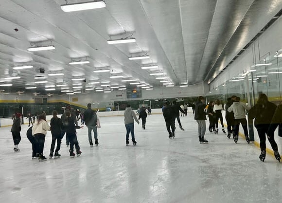 Groups of people ice skate indoors in a rink.