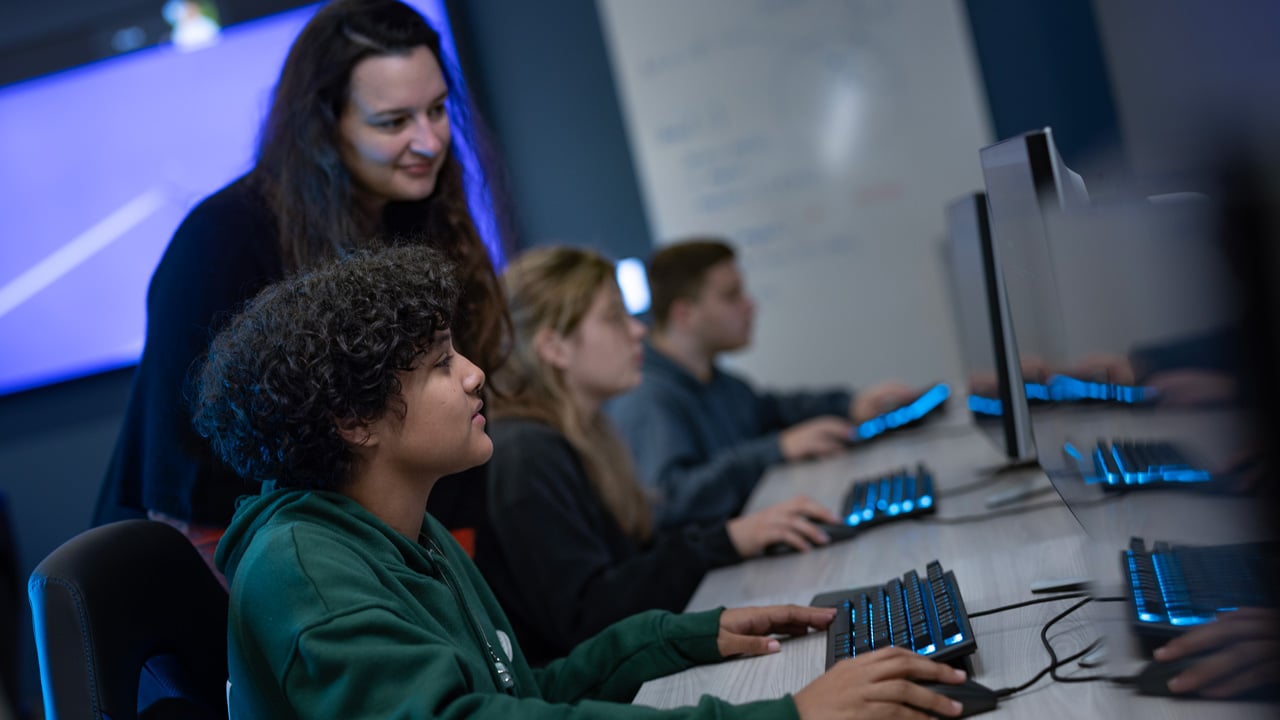 Student working on desktop while a professor looks on