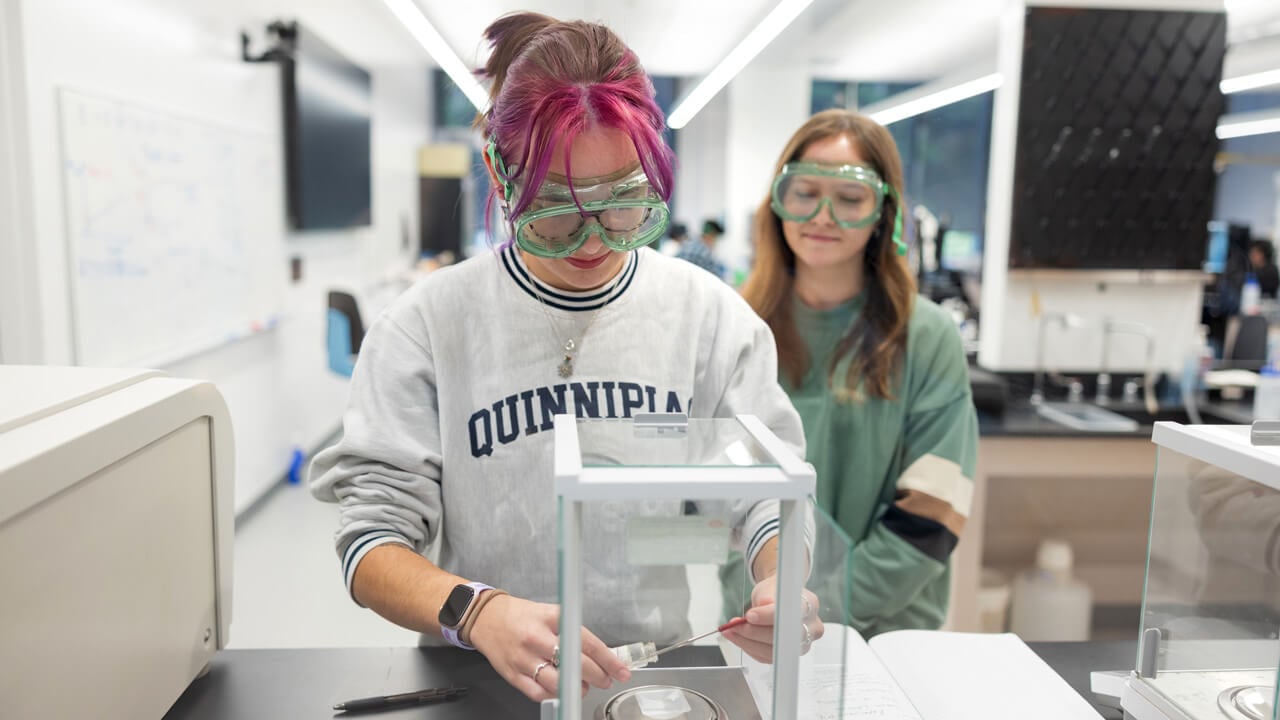 Pair of student wearing safety glasses as they conduct an experiment in a lab