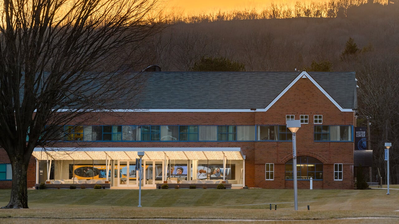 Entrance of Echlin Center windows aglow as the sun sets behind hills in the distance