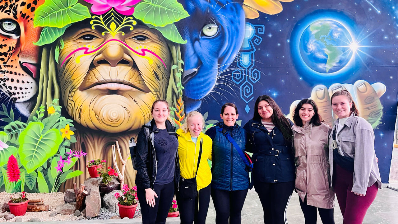 Students pose in front of a colorful mural in Ecuador