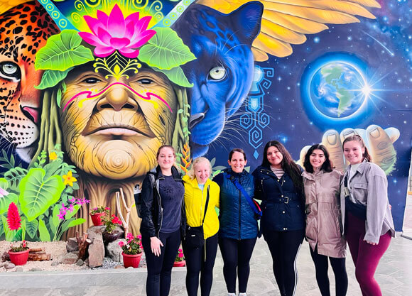 Students pose in front of a colorful mural in Ecuador