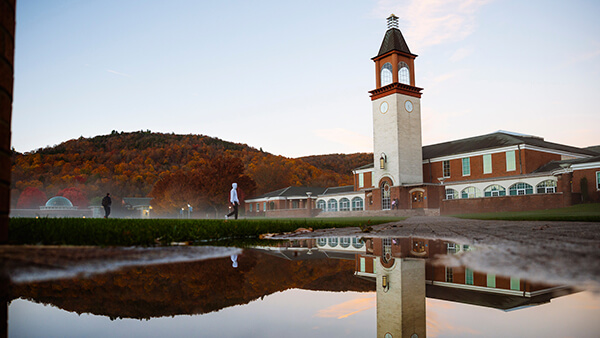 The Arnold Bernhard Library clocktower reflects in a puddle of water on the Mount Carmel Campus quad.