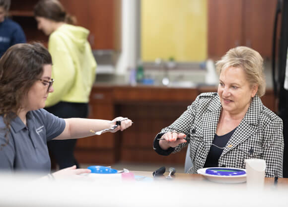An OT professor instructs an OT student using a weighted spoon