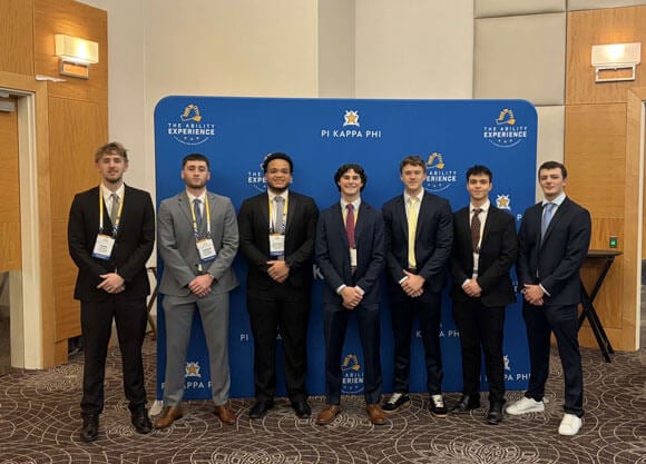 Members of Pi Kappa Phi Iota Lambda chapter smile in front of a blue Pi Kappa Phi step and repeat