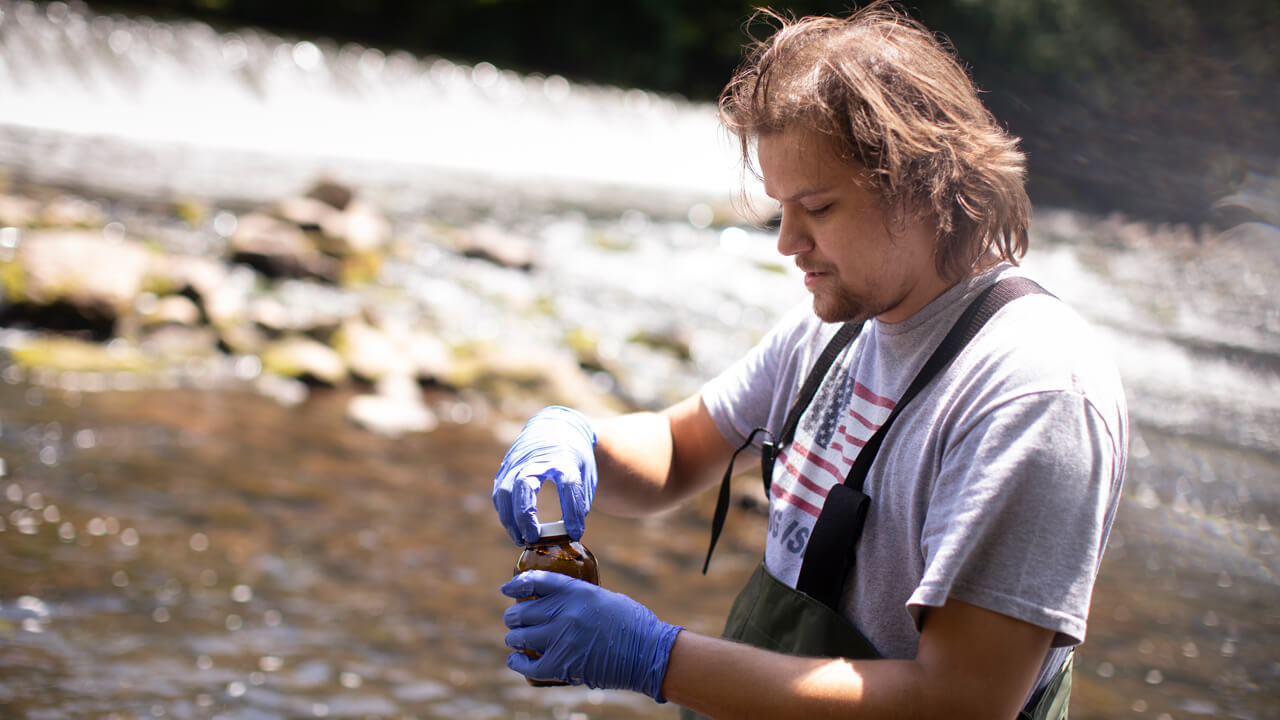 Student collects a water sample from a river during a field study.