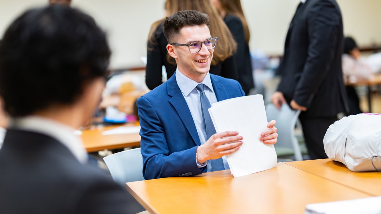 Student holds stack of papers sitting at a table.