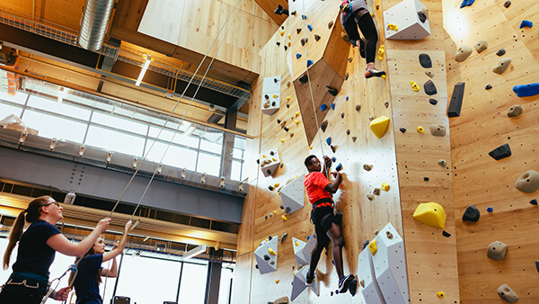 Quinnipiac student climb up the climbing wall in the Recreation and Wellness Center while other student belay them.