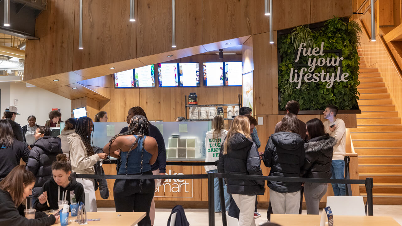 Dozens of students mingle outside the fuel bar with natural wood paneling and living green wall