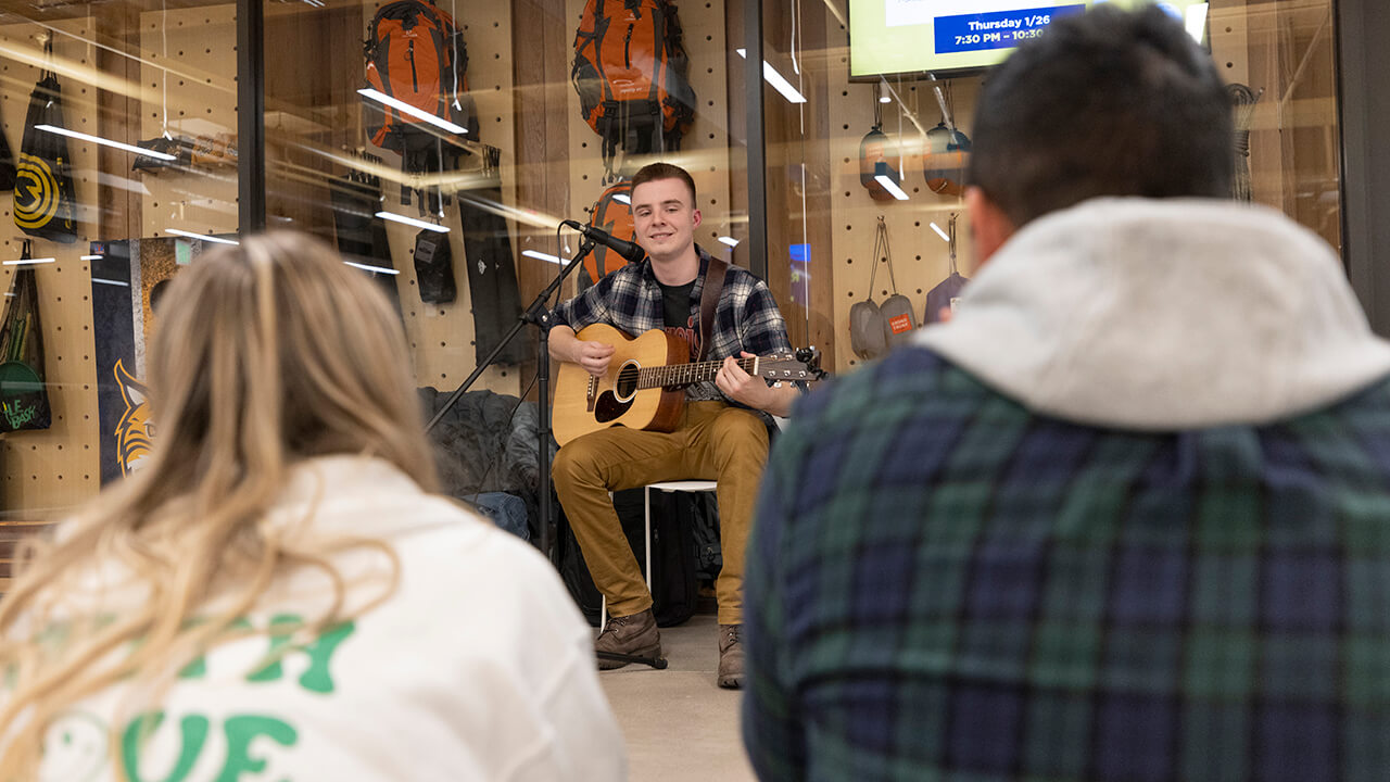 Student plays guitar during rec and wellness center opening.