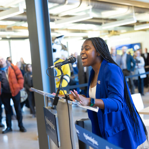 Owenea Roberts smiles as she speaks at a podium during the RecWell opening