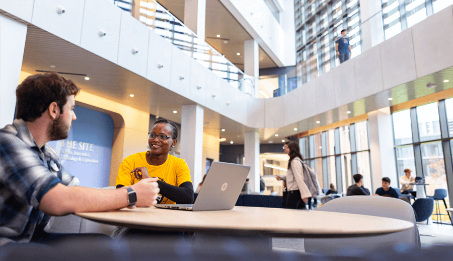 Two students talk together in the 3-story lobby of The SITE