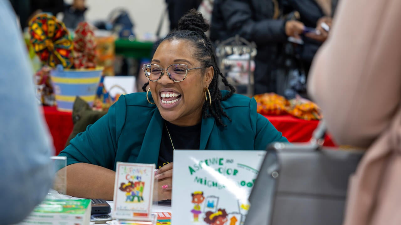 A business owner smiles at a table selling books.
