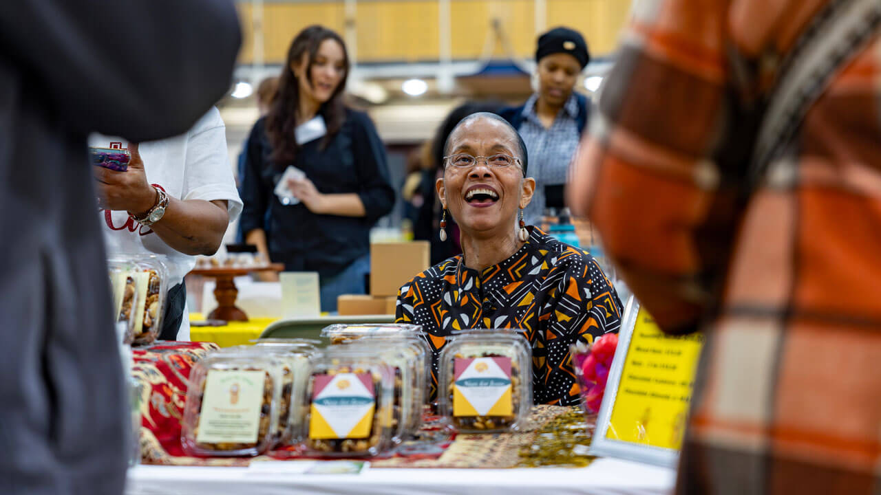 A vendor smiles while selling a food product at their table.