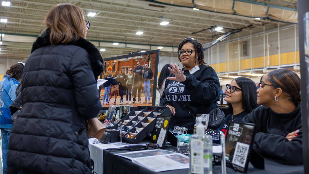 A group of vendors wearing glasses speak to a customer.