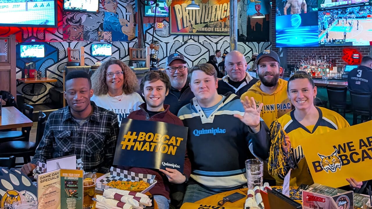 Alumni cheer on Quinnipiac men's ice hockey at a reception.