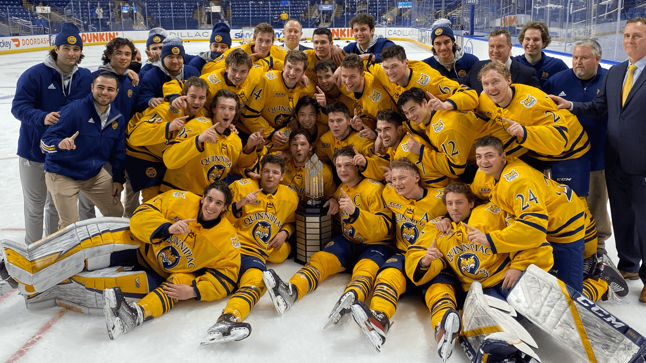 Men's ice hockey team embraces and cheers on the ice with the winning trophy