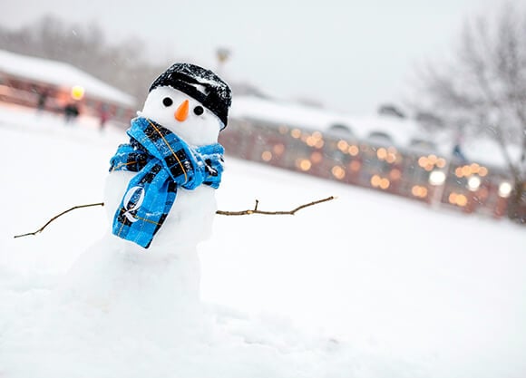 A snowman with a plaid scarf stands in front of an illuminated student center.