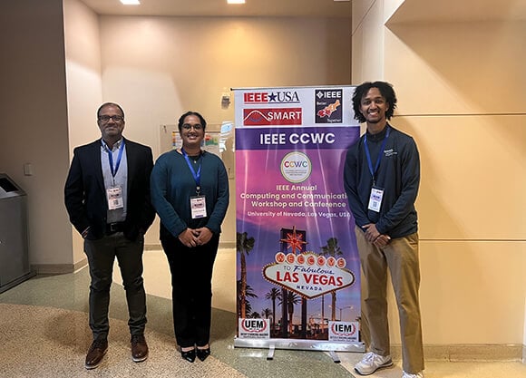 Students and professor standing in front of conference banner